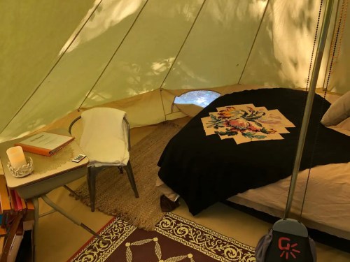 Cozy interior of a tent featuring a bed with a colorful blanket, a chair, and a small table with books.