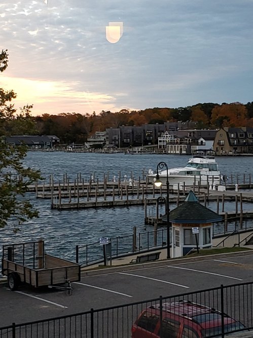 A marina at sunset with a boat docked, surrounded by autumn trees and buildings in the background.