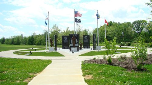 A memorial with flags and statues, surrounded by greenery and a paved walkway, honoring veterans.