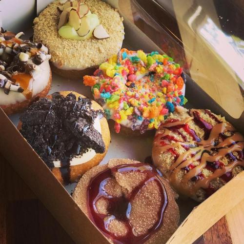 A box of colorful donuts with various toppings, including sprinkles, chocolate, and fruit flavors.