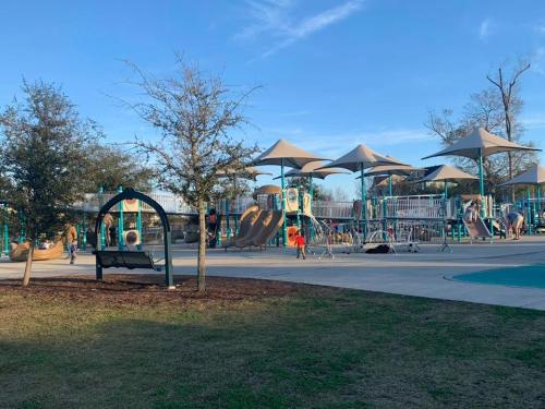 A playground with slides, swings, and shaded areas, surrounded by trees and a clear blue sky.