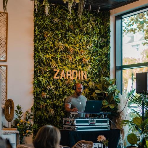 A DJ performs in front of a lush green wall with the name "ZARDIN" displayed prominently.