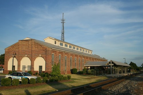 Historic brick building with a police car parked outside, a communication tower in the background, and a train platform nearby.