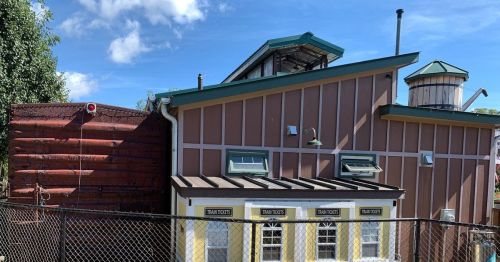 A colorful building with a sloped roof and multiple windows, surrounded by a fence and blue sky in the background.