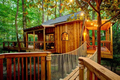 exterior shot of treehouse cabin with netted bridge and warm lighting in the forest