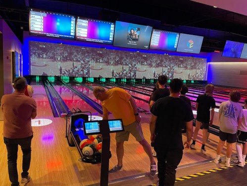 A bowling alley with colorful lights, screens showing a game, and people preparing to bowl.