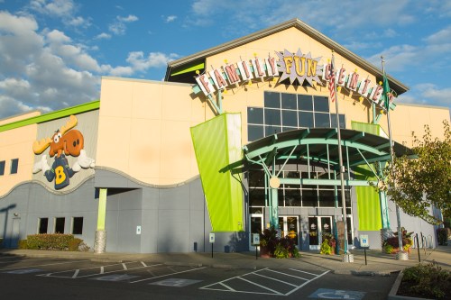 Exterior of a family entertainment center with colorful signage and flags, under a blue sky with clouds.