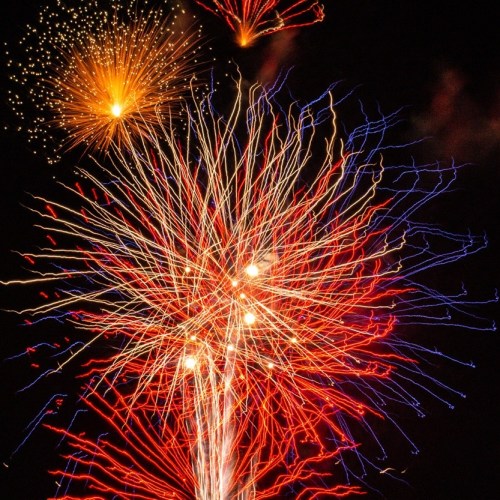 Colorful fireworks explode in the night sky, creating vibrant bursts of red, blue, and gold against a dark background.