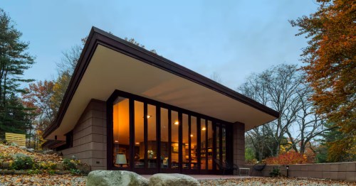 Dramatic view of a modern house with a large overhanging roof and glowing glass windows at night.