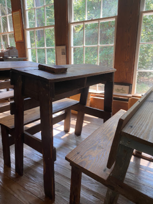 A rustic wooden table and benches in a sunlit room with large windows and wooden floors.