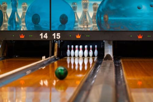 A bowling lane with a green ball rolling towards a set of pins, with blue bowling balls in the background.