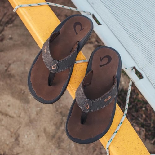 A pair of brown flip-flops resting on a yellow surface, with a sandy background.