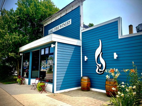 Exterior of Lake Fire Winery, featuring a blue building, large windows, and decorative barrels with flowers in front.