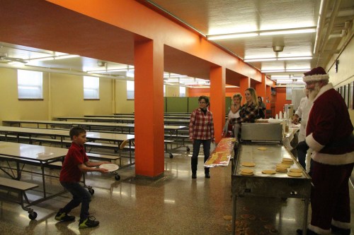 A child throws a plate while Santa and others serve food in a bright, empty cafeteria.