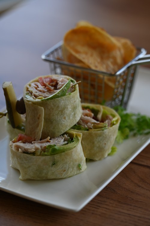 Three rolled wraps filled with chicken, lettuce, and tomato, served with a side of chips in a small basket.