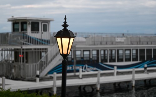 A vintage lamp post illuminates a docked boat at twilight, with calm waters in the background.