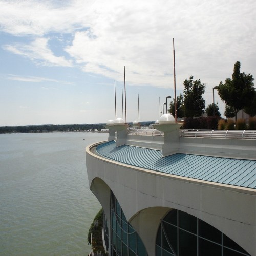 A curved building edge overlooking a calm body of water, with trees and a cloudy sky in the background.
