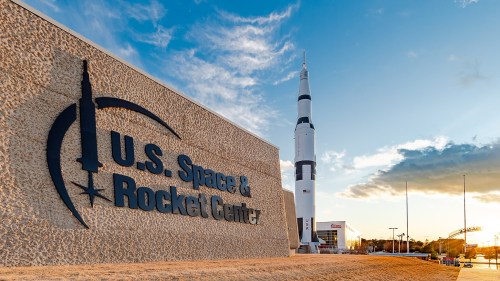 Sign for the U.S. Space & Rocket Center with a large rocket in the background against a sunset sky.