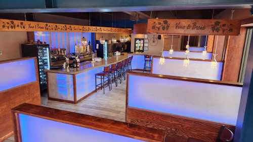 A modern bar interior with blue lighting, wooden accents, and a seating area, creating a cozy atmosphere.