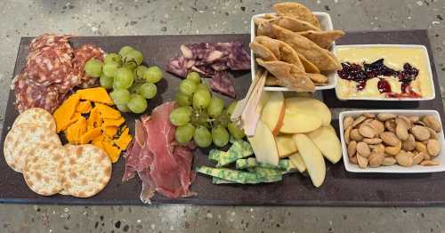 A charcuterie board featuring meats, cheeses, crackers, fruits, and nuts arranged on a dark slate platter.