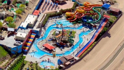 Aerial view of a vibrant water park featuring slides, pools, and lounging areas, with people enjoying the attractions.