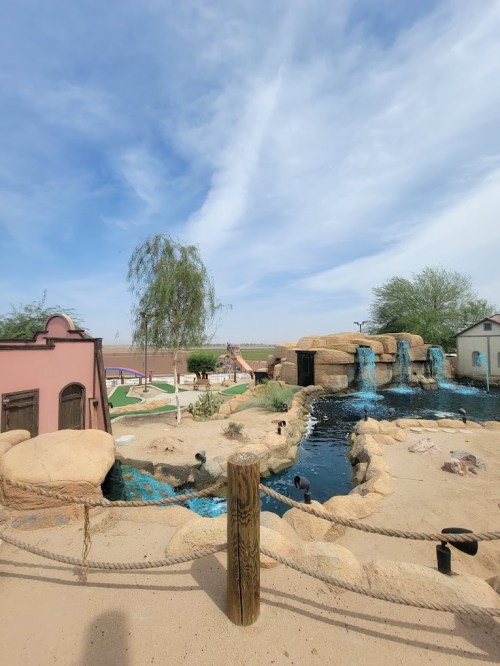 A scenic view of a mini-golf course featuring rocks, water features, and lush greenery under a blue sky.