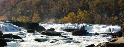 A scenic view of a waterfall cascading over rocks, surrounded by autumn foliage and mist.