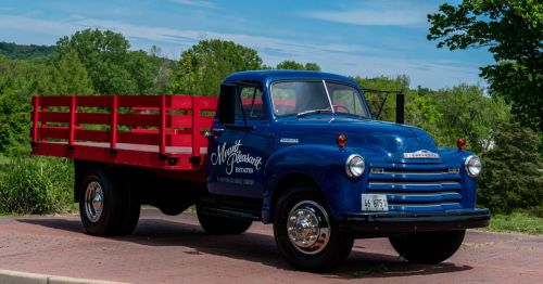 A vintage blue Chevrolet truck with a red wooden flatbed, with greenery in the background in wine country in Missouri.
