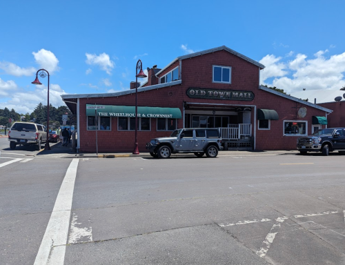 A red building with a green awning labeled "The Wheelhouse & Crownwest" at Old Town Mall, with cars parked outside.