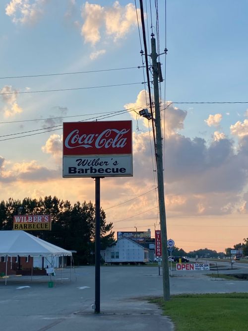 Sign for Wilber's Barbecue with a Coca-Cola logo, set against a cloudy sky at dusk.