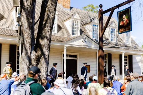 A historical reenactment outside a colonial-style building, with a crowd watching and actors in period costumes.