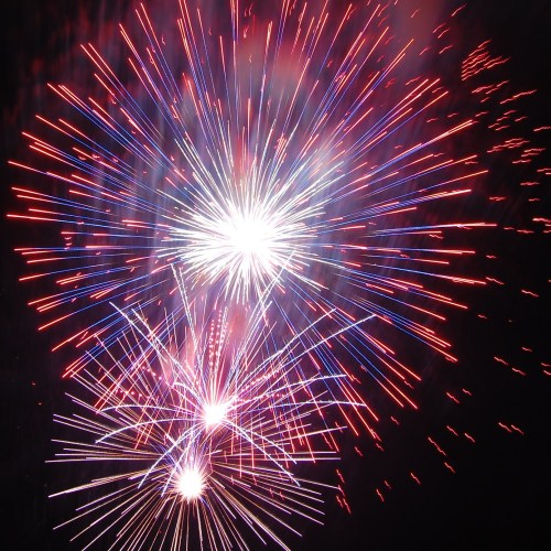 Colorful fireworks explode in the night sky, creating vibrant bursts of red, blue, and white light.
