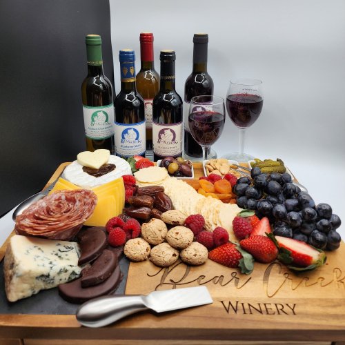 A beautifully arranged charcuterie board with cheeses, meats, fruits, cookies, and wine bottles and glasses.