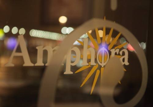 A close-up of a glass door featuring the word "Amphora" and a sunburst design, with blurred lights in the background.