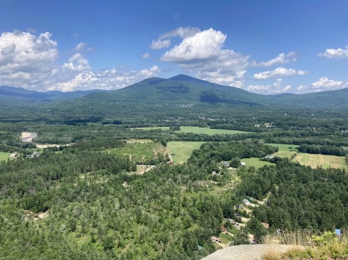 A panoramic view of lush green valleys and mountains under a blue sky with fluffy clouds.