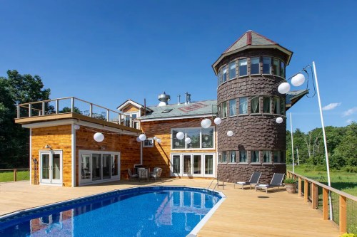 A modern house with a tower, surrounded by a deck and pool, featuring decorative lanterns and a clear blue sky.