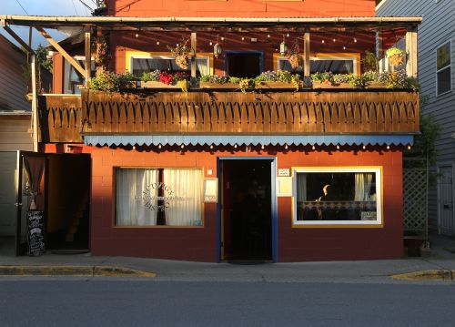 A colorful two-story building with a flower-adorned balcony and large windows, located on a street corner.