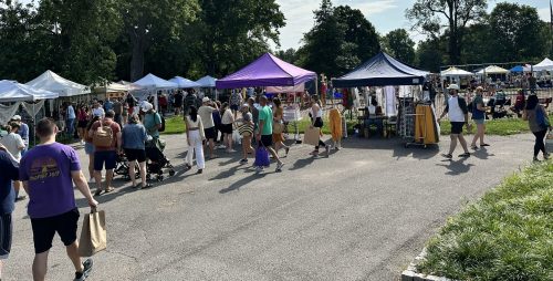A bustling outdoor market with colorful tents, vendors, and crowds of people enjoying the sunny day.