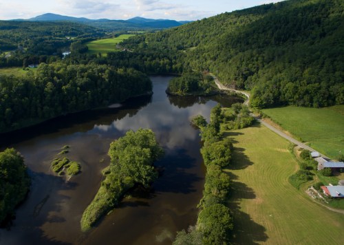 Aerial view of a serene river winding through lush green hills and fields under a partly cloudy sky.