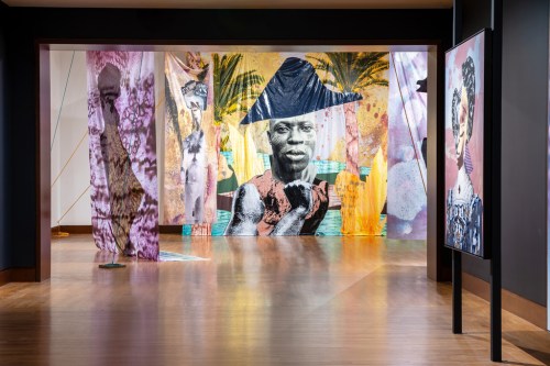 Colorful art installation featuring large fabric prints of figures and vibrant backgrounds in a gallery setting.