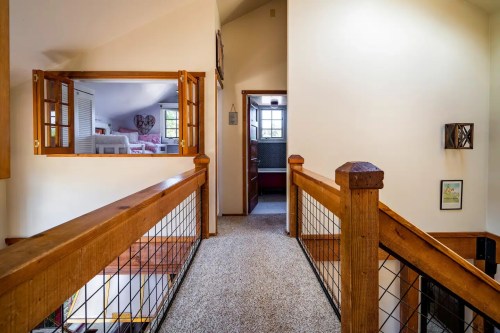 A cozy hallway with wooden railings, leading to rooms with doors and a view of a bright living space.