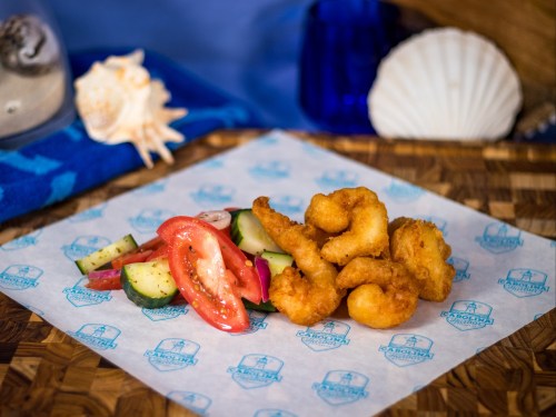 A plate of golden fried shrimp served with a fresh salad of cucumbers and tomatoes on a decorative paper.