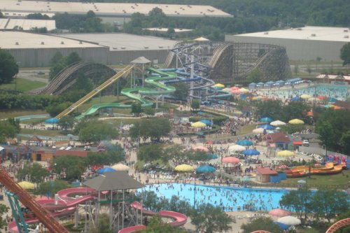 Aerial view of a water park with slides, a wave pool, and colorful umbrellas, bustling with visitors on a sunny day.