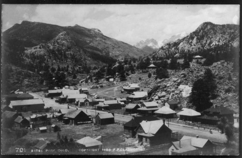 Black and white photo of a small mountain town surrounded by hills and trees, with buildings scattered throughout.