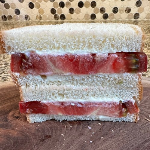 A sandwich with layers of tomato and mayonnaise between two slices of white bread, resting on a wooden surface.