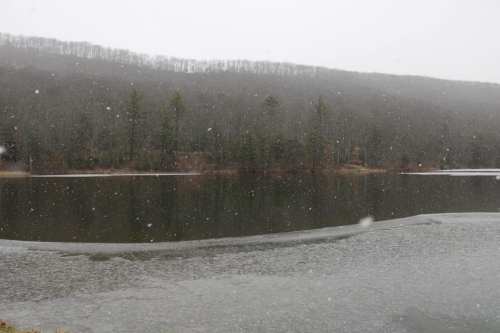 A snowy landscape with a lake and forested hills in the background, creating a serene winter scene.
