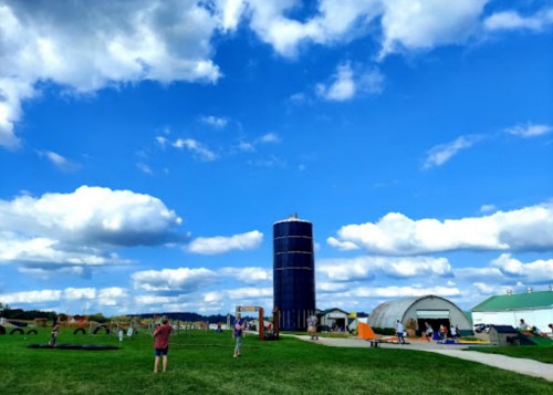 A sunny farm scene with children playing, a tall silo, and various buildings under a blue sky with fluffy clouds.