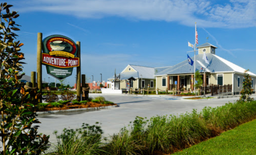 A building with a sign reading "Adventure Point," surrounded by greenery and flags, under a clear blue sky.