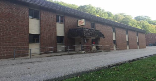 A brick building with a sloped roof and a sign reading "Student Housing Store," surrounded by greenery.