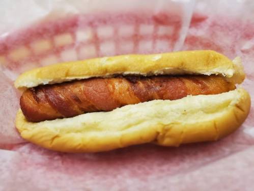 A close-up of a hot dog in a soft bun, resting on pink paper in a basket.